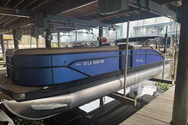 Slide: The Image of 2023 Barletta Cabrio 24CC pontoon boat docked under a covered marina. - 0