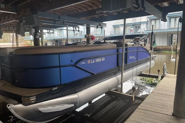 Slide: The Image of 2023 Barletta Cabrio 24CC pontoon boat docked under a covered marina. - 1