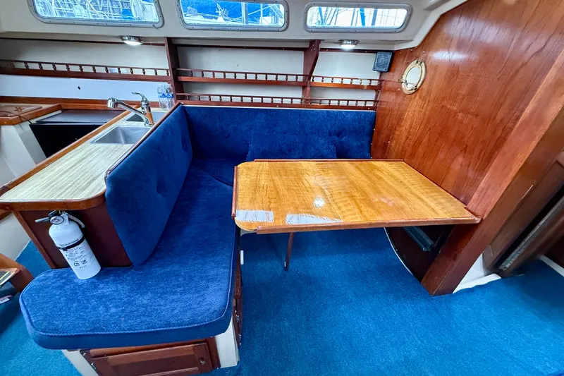 Slide: The Image of 1982 Catalina 30 sailboat interior with blue seating, wooden table, and kitchenette. - 19