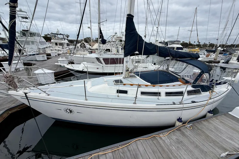 Slide: The Image of 1982 Catalina 30 sailboat docked at marina, surrounded by other boats under cloudy skies. - 2