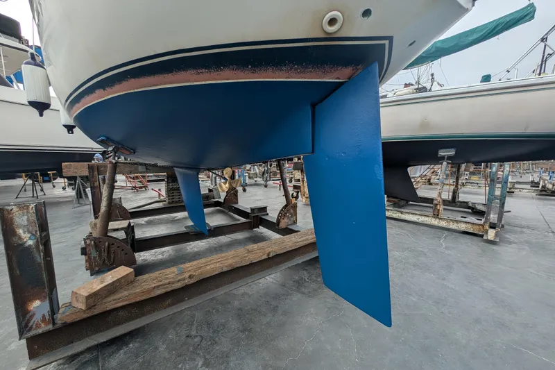 Slide: The Image of 1982 Catalina 30 sailboat on stands, showcasing blue keel and rudder in a boatyard. - 38
