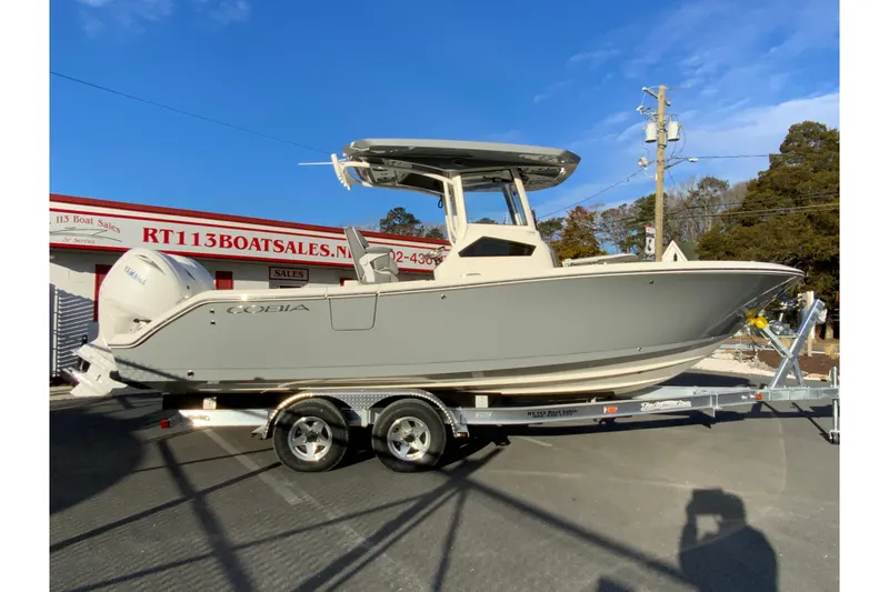 The Image of 2026 Cobia 245 Center Console boat on trailer at dealership, clear sky background. - 1