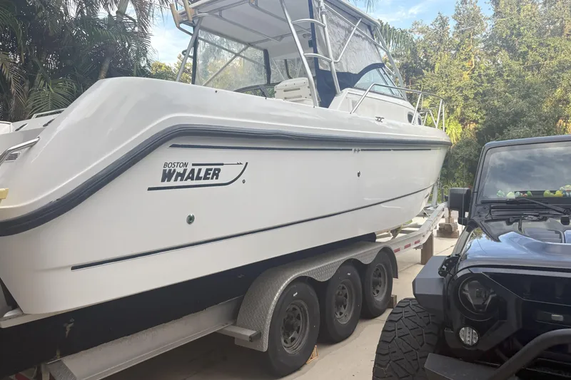 The Image of 2001 Boston Whaler 285 Conquest boat on trailer beside a black vehicle. - 0