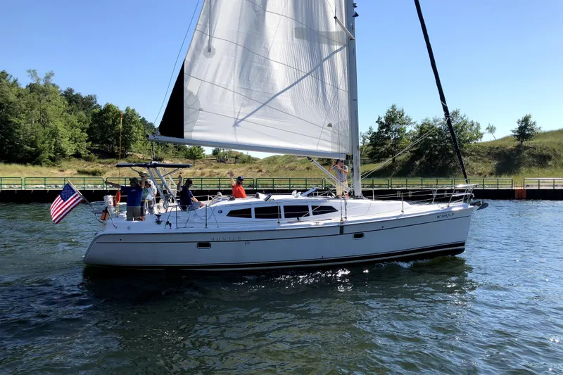 The Image of 2011 Hunter 39 sailboat on water with American flag, surrounded by greenery. - 0