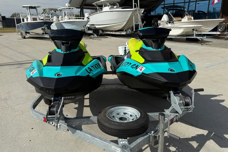 Slide: The Image of 2022 Sea-Doo Spark 3up jet skis on trailer, vibrant colors, parked outdoors. - 2