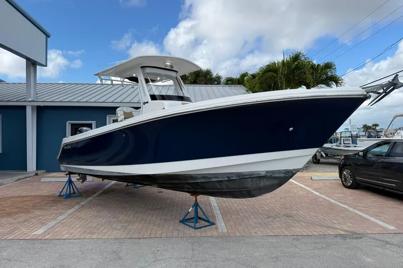 Slide: The Image of 2018 Edgewater 262CC boat on stands, blue hull, parked outdoors. - 6
