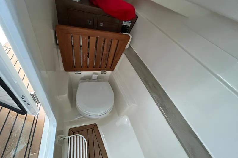 Slide: The Image of 2022 Boston Whaler 320 Vantage boat interior with compact marine toilet and wooden accents. - 12