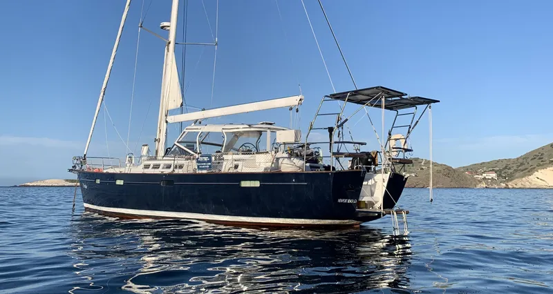 Slide: The Image of 2005 Beneteau 57 sailboat anchored in calm waters, clear sky, coastal background. - 2