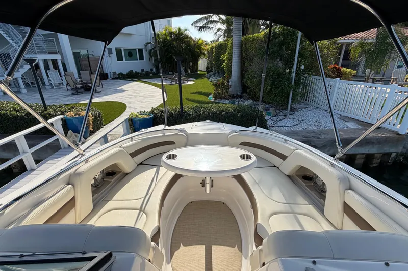 Slide: The Image of 2015 Chaparral 264 Sunesta boat interior with seating and table, docked near a landscaped yard. - 10