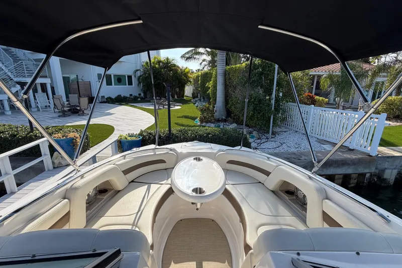 Slide: The Image of 2015 Chaparral 264 Sunesta boat interior with seating and table, docked near a landscaped yard. - 11