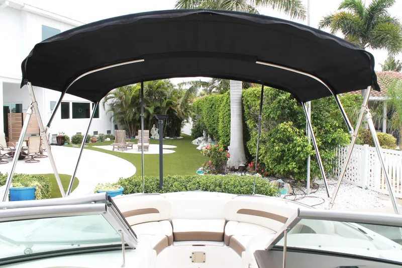 Slide: The Image of 2015 Chaparral Sunesta 264 boat with canopy, parked near a lush garden and modern house. - 32