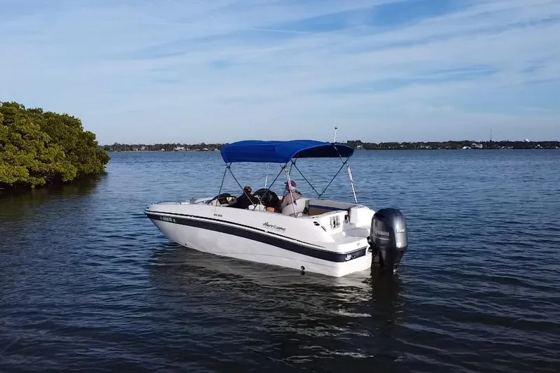 Slide: The Image of 2018 Hurricane Sundeck Sport 218 OB boat on calm water with blue canopy. - 18