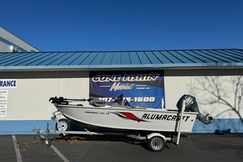 The Image of 2010 Alumacraft Fisherman 145 CS boat on trailer, parked outside a building under clear blue sky. - 1