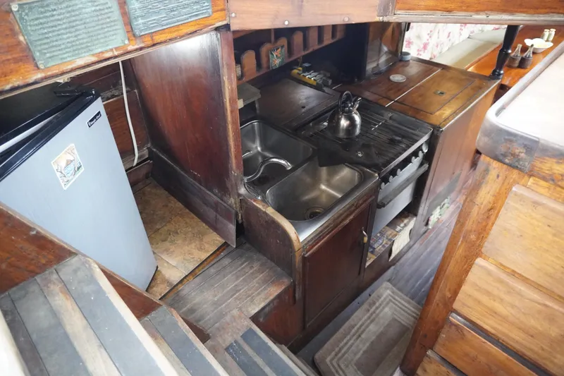 Slide: The Image of 1976 Manila Shipbuilders sailboat kitchen with wooden cabinetry, sink, stove, and compact refrigerator. - 39