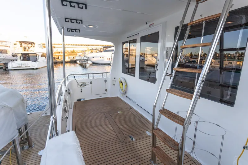 Slide: The Image of 2021 North Pacific 49 Pilothouse yacht deck with wooden flooring and ladder, docked at marina. - 26