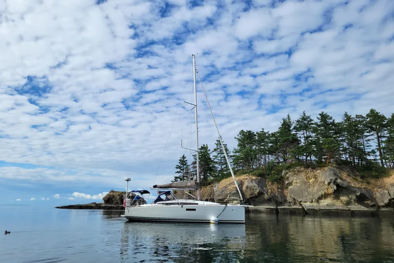 Slide: The Image of 2017 Jeanneau Sun Odyssey 349 sailboat anchored near rocky shoreline under cloudy sky. - 19