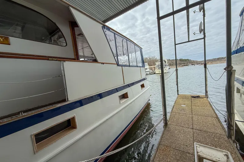 Slide: The Image of 1956 Burger Pilothouse yacht docked by a serene lake under a cloudy sky. - 4