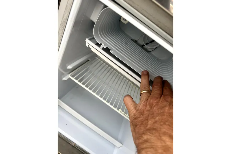 Slide: The Image of Hand inspecting a refrigerator inside a 2018 Scout 350 LXF boat. - 25