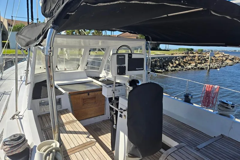 Slide: The Image of 1982 Tayana Center Cockpit Cutter Ketch with covered helm, docked by rocky shoreline. - 21