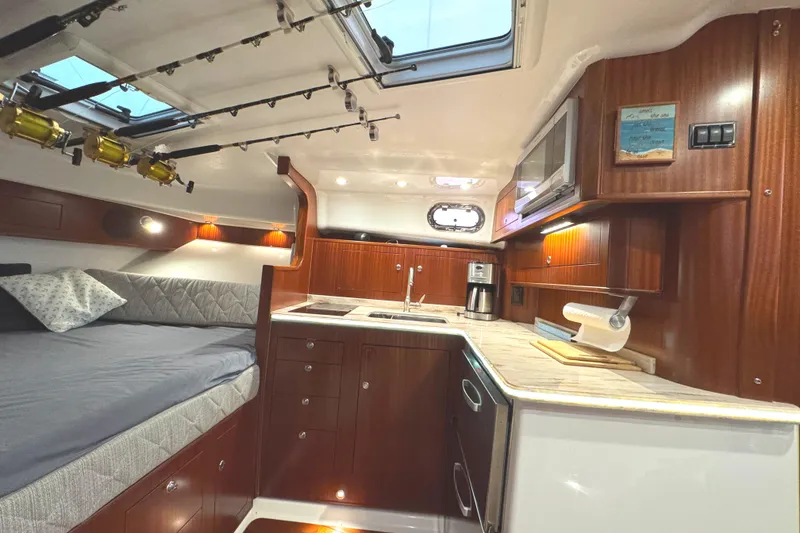 Slide: The Image of 2019 Pursuit OS 385 Offshore cabin with kitchen, bed, and fishing rods. - 11