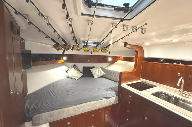 Slide: The Image of 2019 Pursuit OS 385 Offshore cabin interior with fishing rods, bed, and kitchenette. - 13