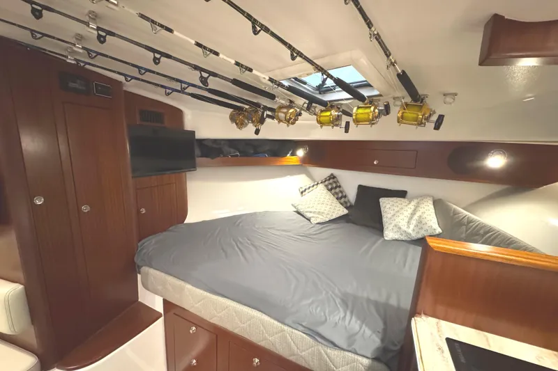 Slide: The Image of 2019 Pursuit OS 385 Offshore cabin with fishing rods, cozy bed, and wooden cabinetry. - 14
