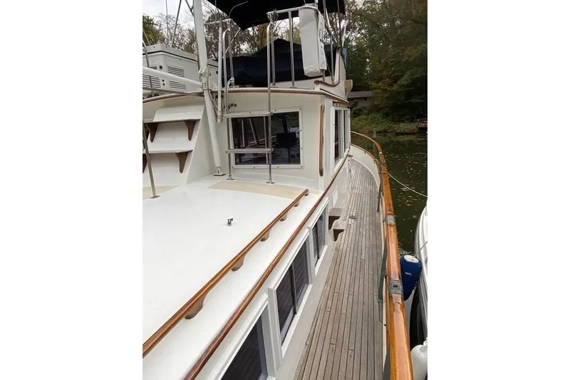 Slide: The Image of 1981 Grand Banks 36 Classic yacht with wooden deck and railing, docked by a wooded shoreline. - 10