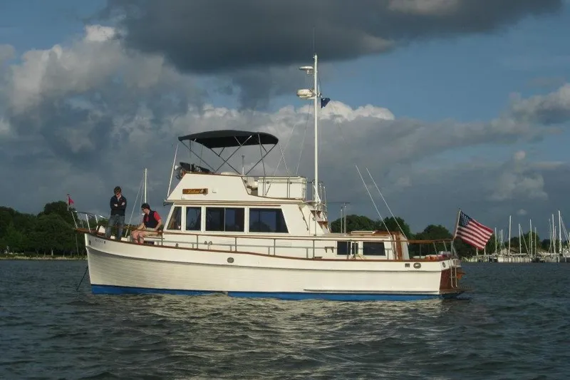 Slide: The Image of 1981 Grand Banks 36 Classic yacht on water, with people on deck, under cloudy sky. - 5