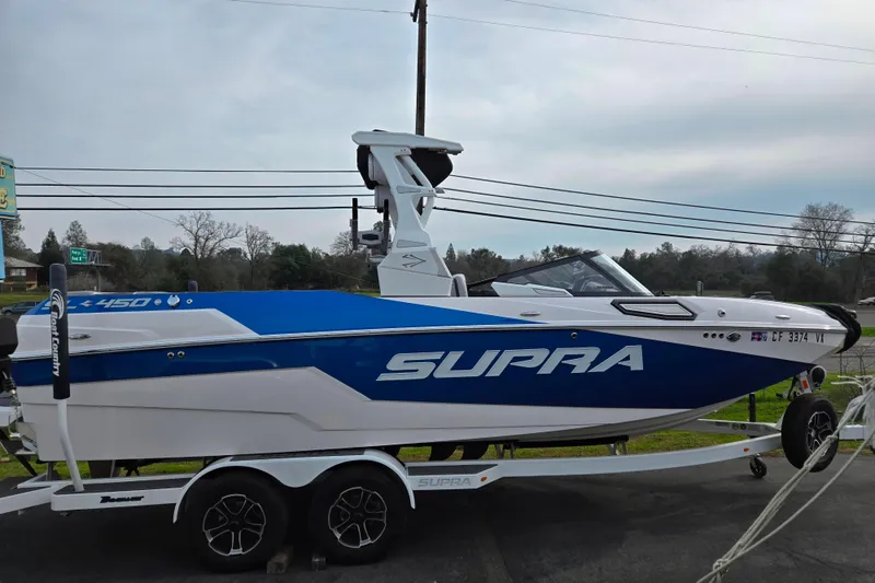 The Image of 2023 Supra SL 450 boat on trailer, blue and white design, parked outdoors. - 1