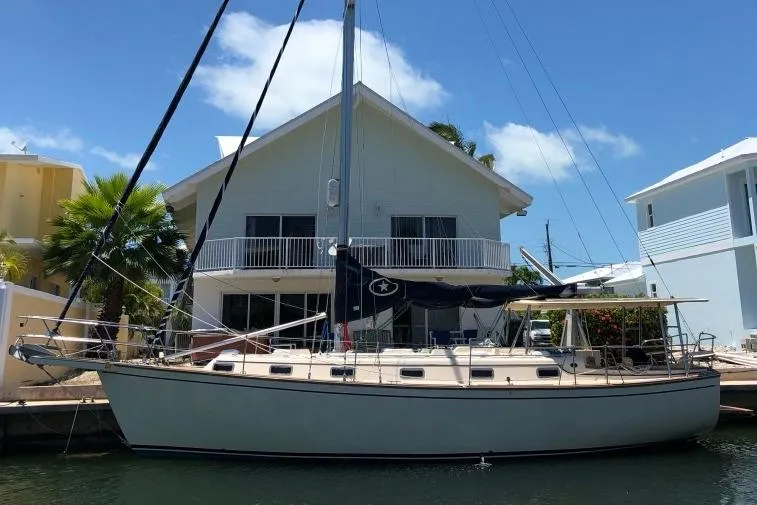 The Image of 1989 Island Packet 38 sailboat docked by a waterfront house under a clear blue sky. - 0