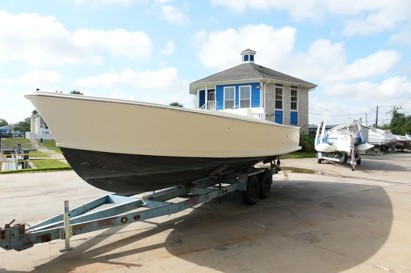 The Image of 1978 Bertram 31 Sportfisher boat on trailer, parked near a blue building. - 0
