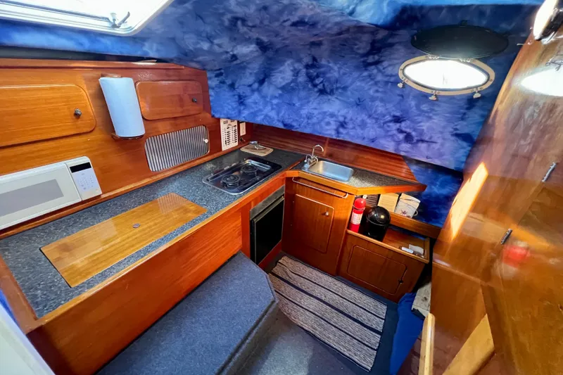 Slide: The Image of 1998 Baha Cruisers 340 CAT boat interior with kitchenette, featuring wood cabinetry and blue accents. - 40