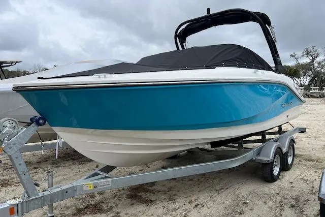 The Image of 2026 Bayliner V20 boat on trailer, blue hull, black cover, parked on sandy ground. - 1