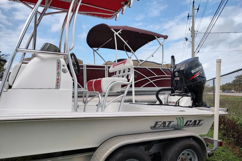 Slide: The Image of 2016 Fat Cat 21 boat on trailer beside pontoon, under cloudy sky. - 9