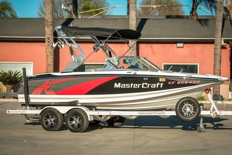 The Image of 2013 MasterCraft X-2 boat on trailer, black and red design, parked outdoors. - 1