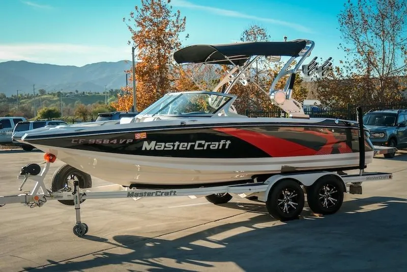 Slide: The Image of 2013 MasterCraft X-2 boat on trailer, parked outdoors with scenic mountain backdrop. - 4