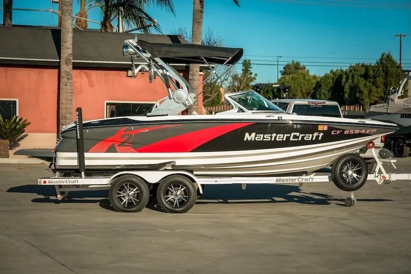 Slide: The Image of 2013 MasterCraft X-2 boat on trailer, parked outdoors, with palm trees in the background. - 7