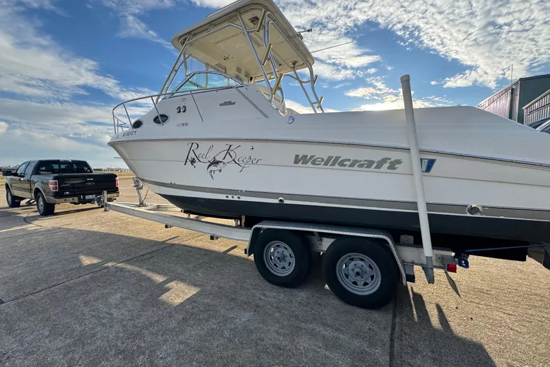 Slide: The Image of 2009 Wellcraft 270 Coastal O/B boat on trailer, parked beside a truck under a blue sky. - 14