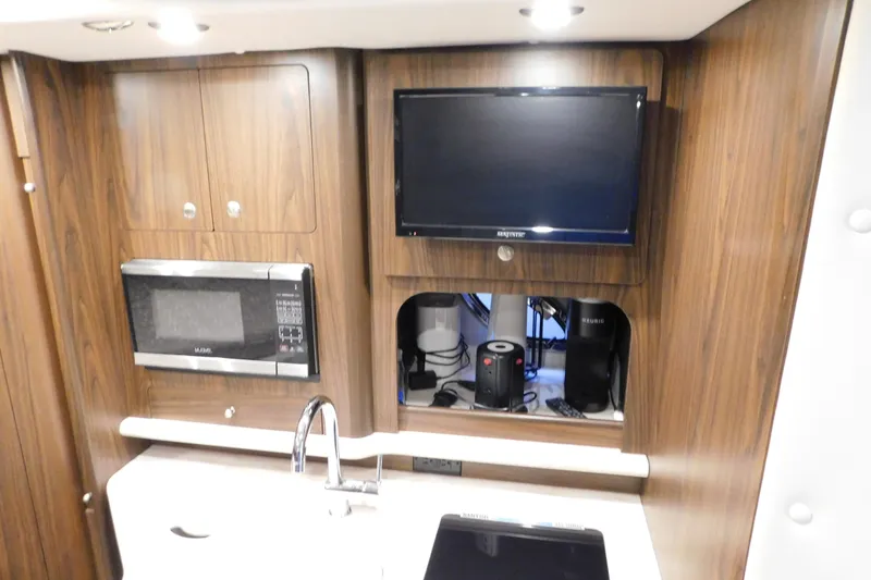 Slide: The Image of 2017 Rinker EX 320 interior with microwave, TV, and sink in wooden cabinetry. - 76