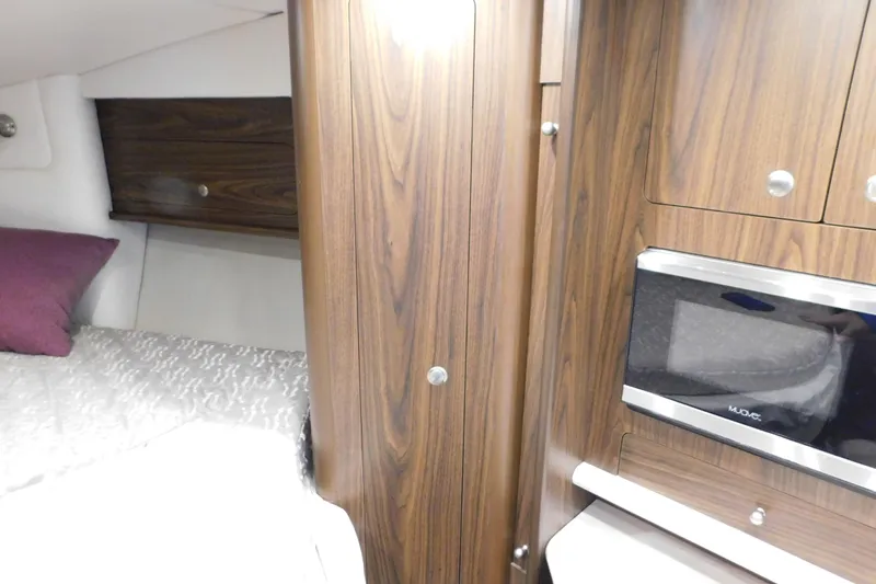 Slide: The Image of 2017 Rinker EX 320 cabin interior with wood paneling, bed, and microwave. - 81