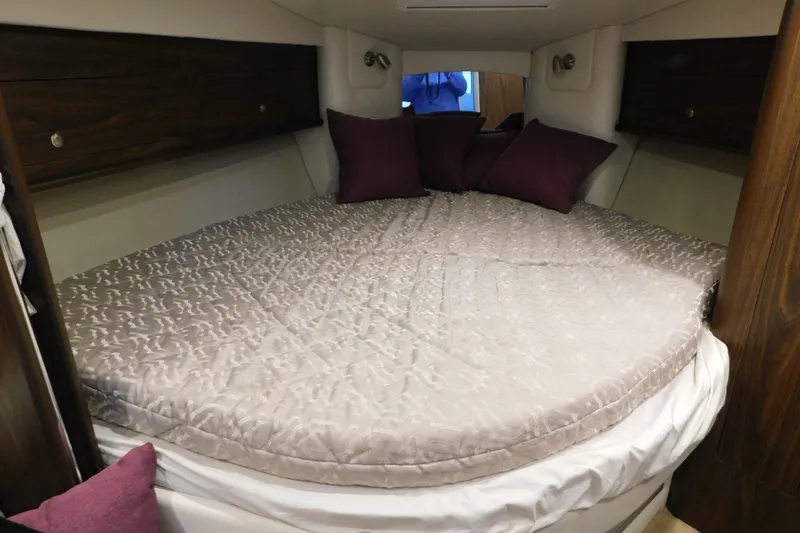 Slide: The Image of 2017 Rinker EX 320 cabin interior with cozy bed and purple pillows. - 91
