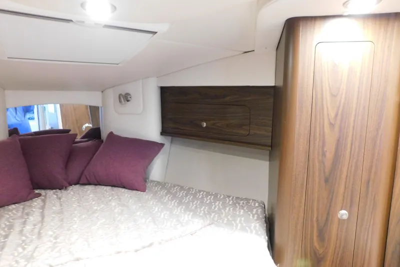 Slide: The Image of 2017 Rinker EX 320 cabin interior with bed, pillows, and wooden cabinetry. - 92
