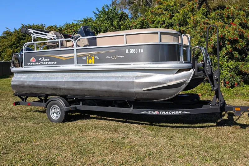 The Image of 2025 Sun Tracker Party Barge 16 DLX pontoon boat on trailer, parked on grass. - 1