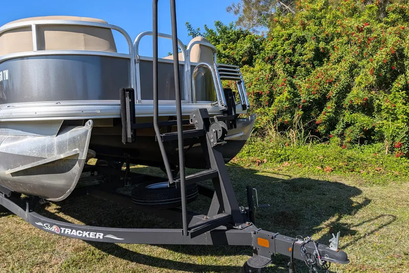 Slide: The Image of 2025 Sun Tracker Party Barge 16 DLX pontoon boat on trailer, surrounded by greenery. - 5