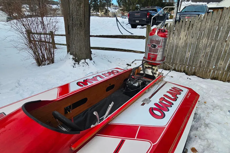 Slide: The Image of 1987 De Silva F Class Race boat in snow, featuring "Outlaw" design and vintage outboard motor. - 2
