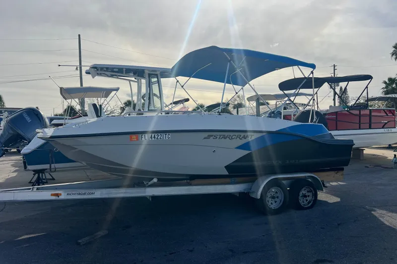 The Image of 2022 Starcraft SVX 191 OB boat on trailer with blue canopy in a marina. - 0