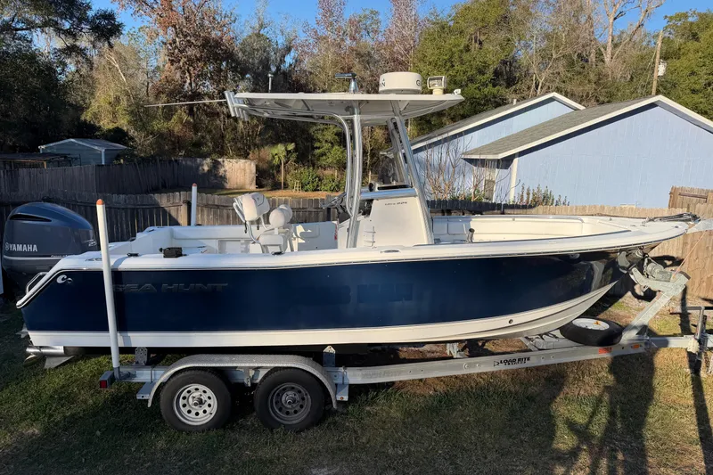 Slide: The Image of 2015 Sea Hunt Ultra 225 boat on trailer, parked in a yard with trees and a house. - 15