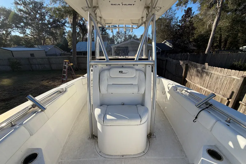 Slide: The Image of 2015 Sea Hunt Ultra 225 boat interior with seating and console, in a backyard setting. - 50