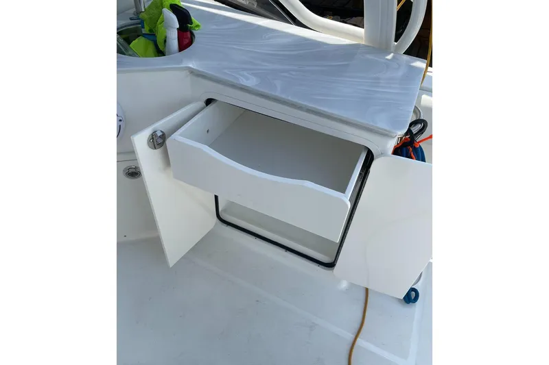 Slide: The Image of Open storage compartment on 2023 World Cat 280 DC-X boat, featuring a drawer and cleaning supplies. - 11