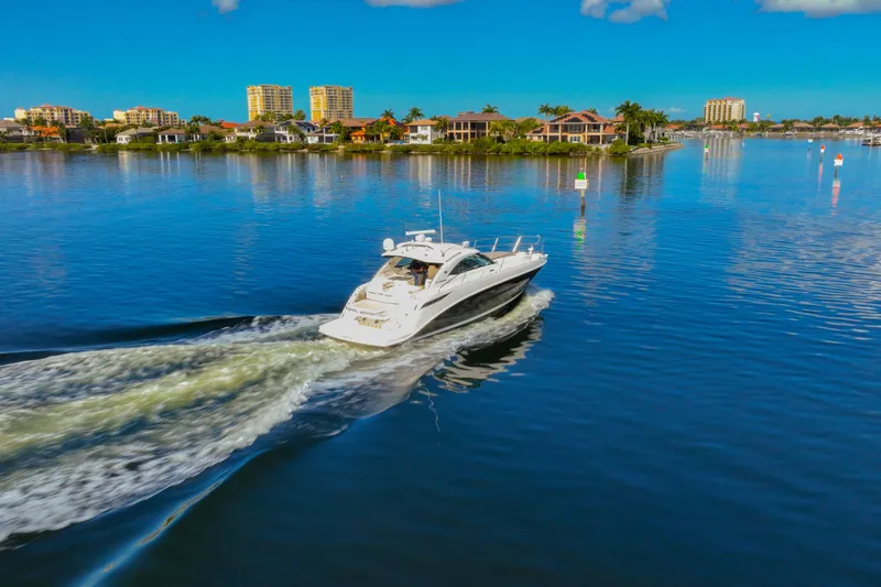 Slide: The Image of 2015 Sea Ray 410 Sundancer cruising on a serene waterway with cityscape backdrop. - 13